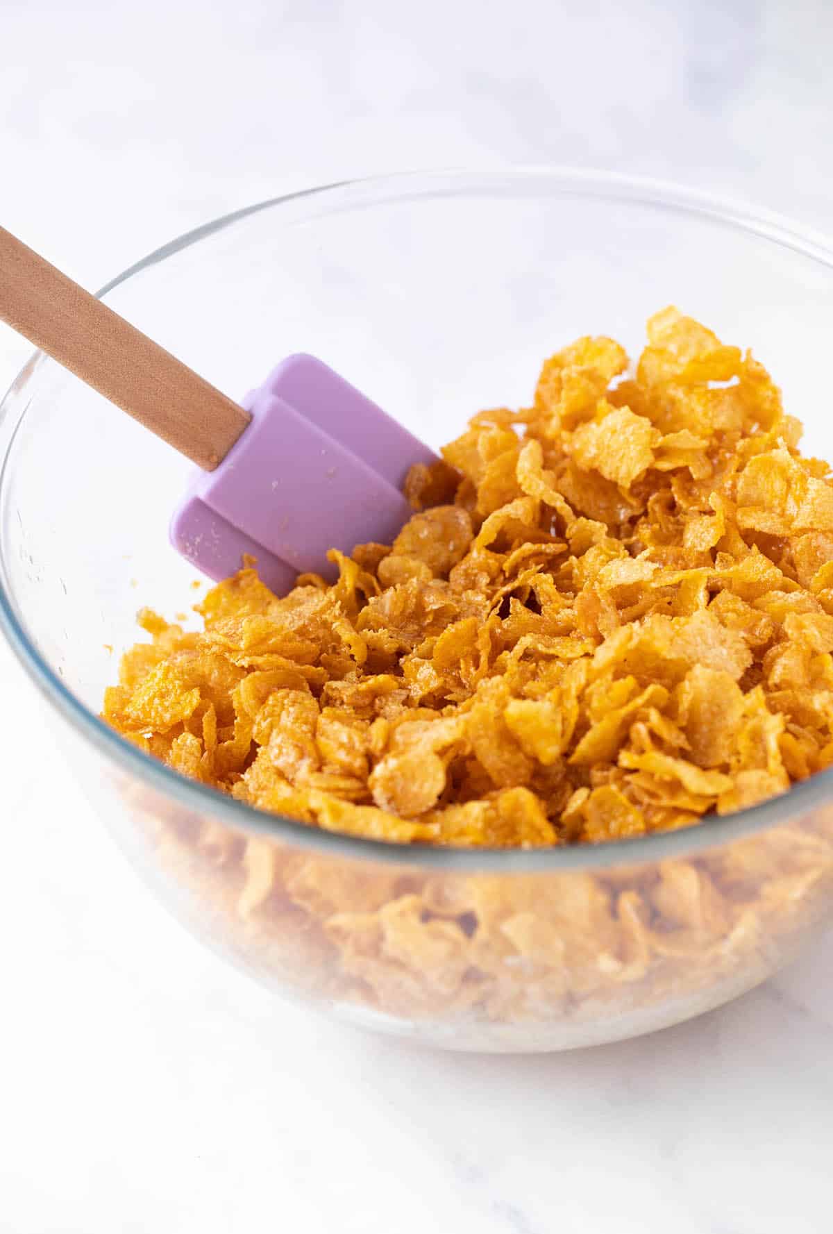 A bowl of cornflakes with a purple spatula.