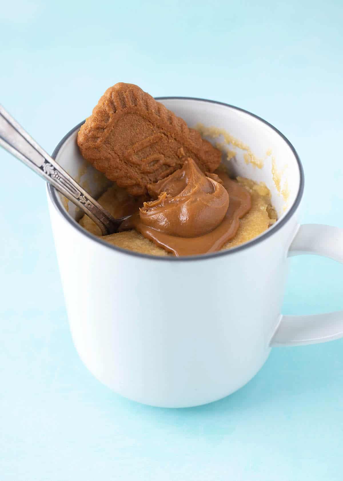Biscoff Mug Cake topped with Biscoff on a blue background.