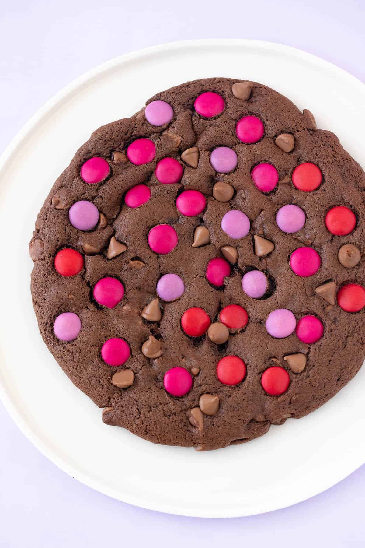 A giant chocolate cookie decorated with pink and purple candies.