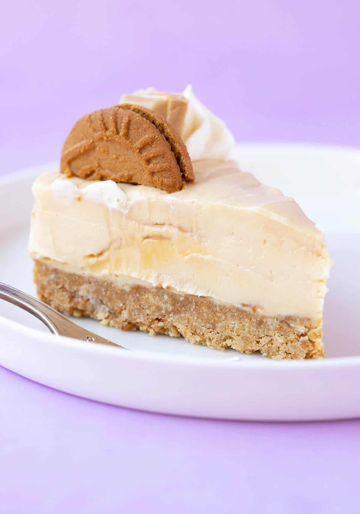 A slice of no bake Caramilk Cheesecake on white plate with a purple background.