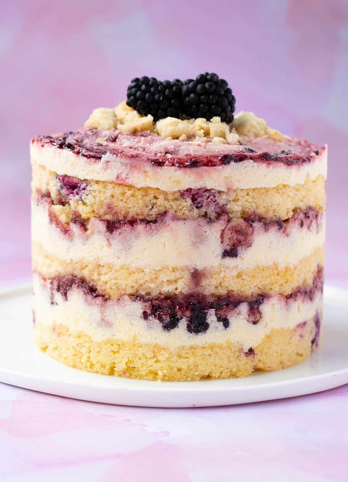 A stunning Lemon Blackberry Cake frosted in Milk Bar style on a white plate. 