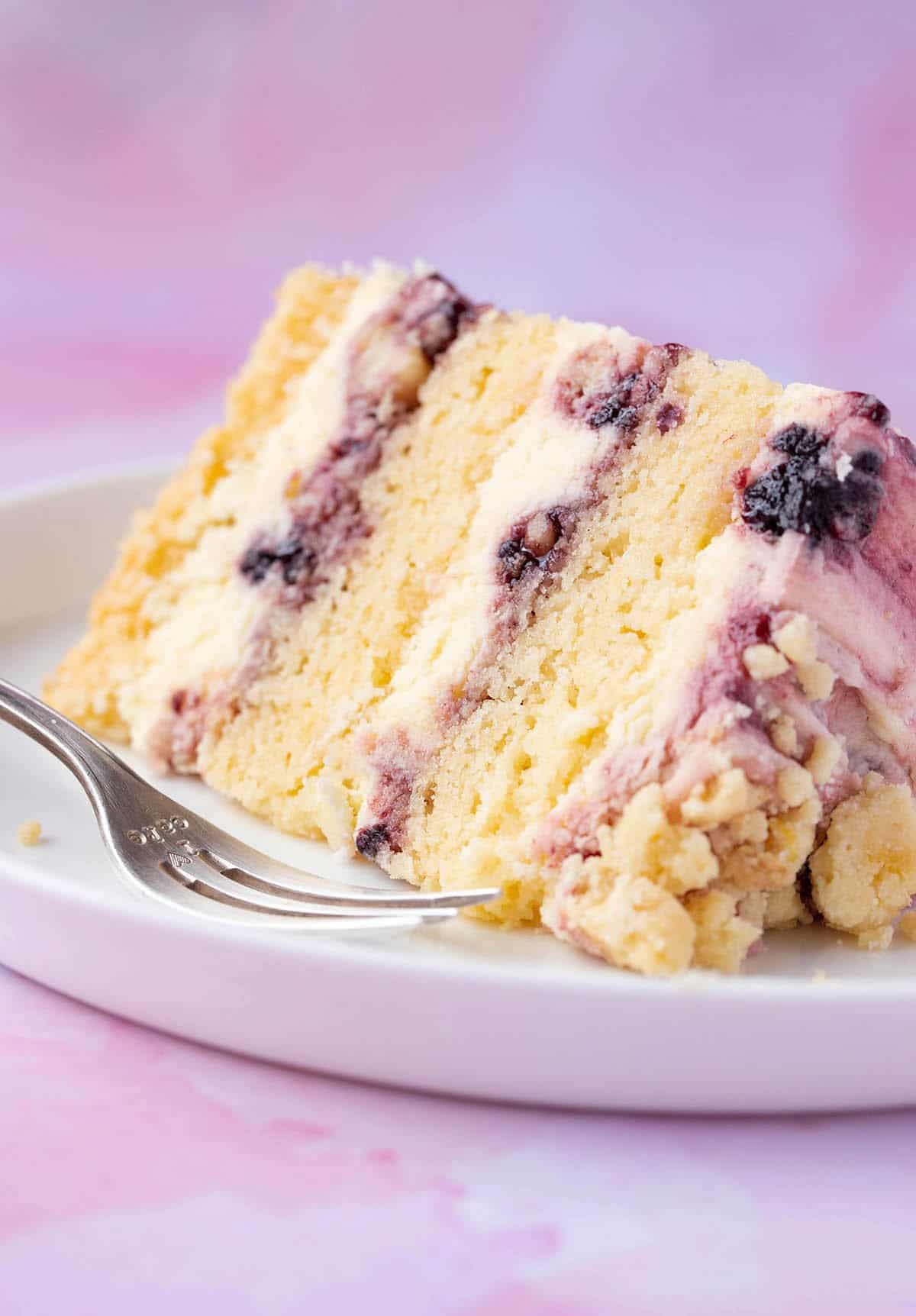 A slice of Lemon Blackberry Cake on a purple background. 