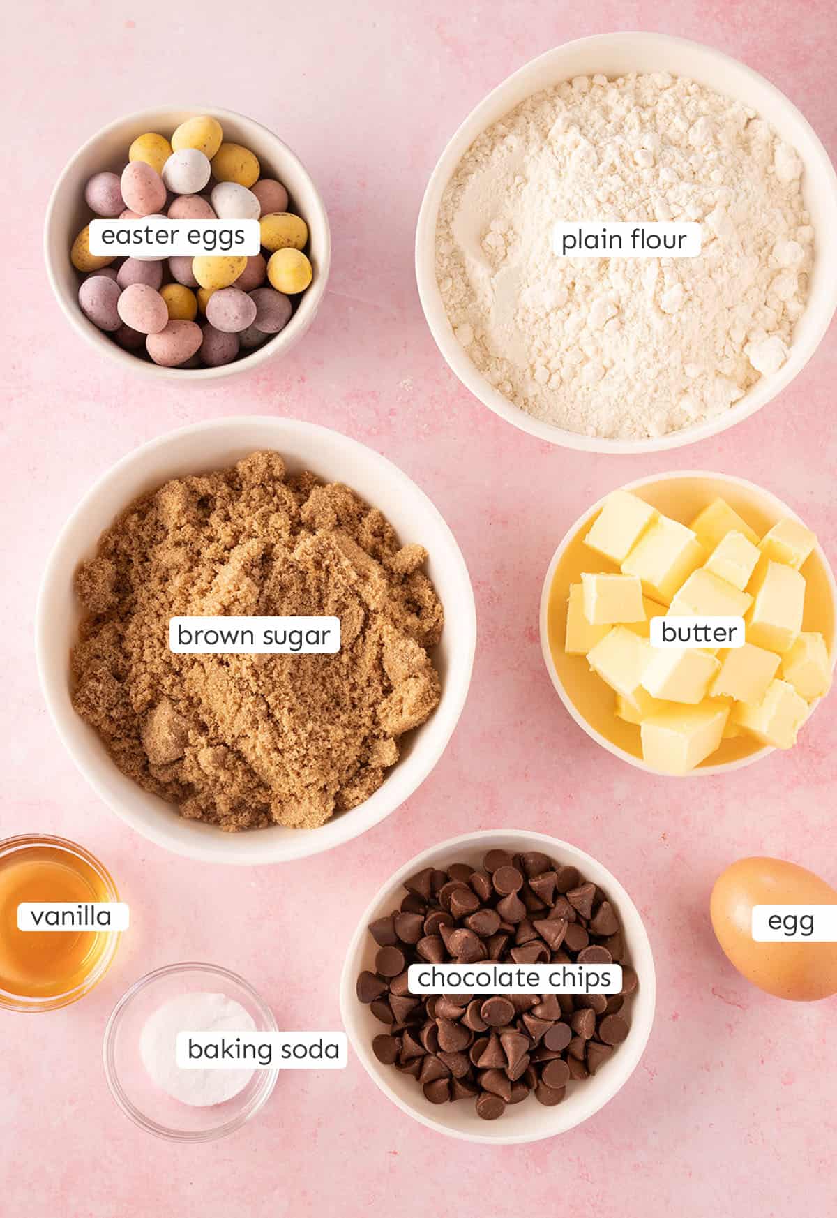 All the ingredients needed to make Mini Egg Cookies from scratch on a pink backedrop.