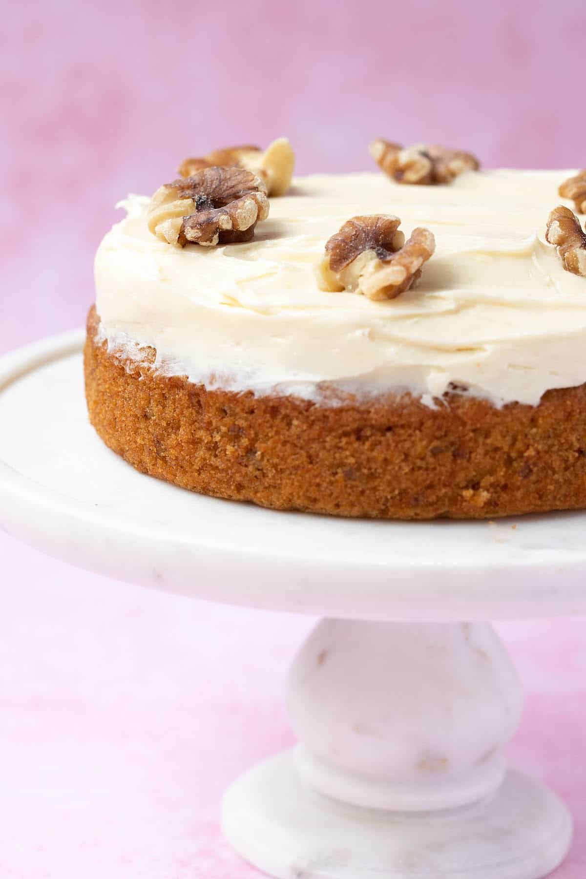 A small 6-inch Carrot Cake topped with cream cheese frosting on a white cake stand.