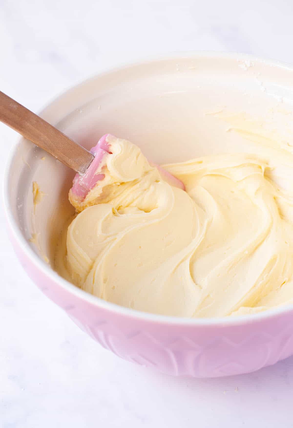 A pink mixing bowl filled with white chocolate buttercream. 