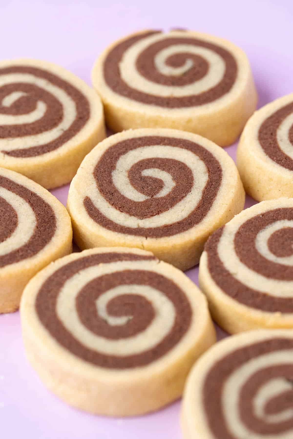 Close up of vanilla and chocolate swirl cookies on a pink background.