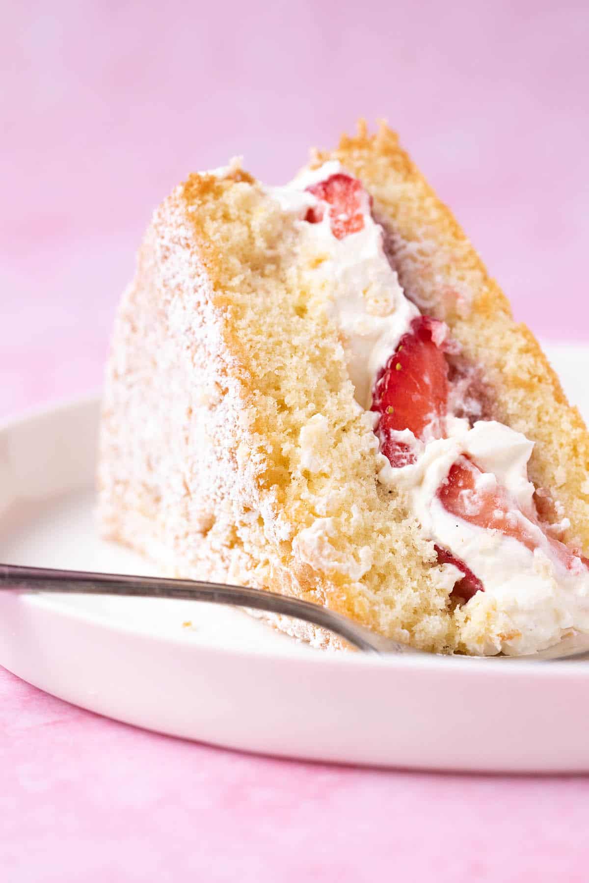 A slice of Sponge Cake filled with strawberries on a white plate with a cake fork.