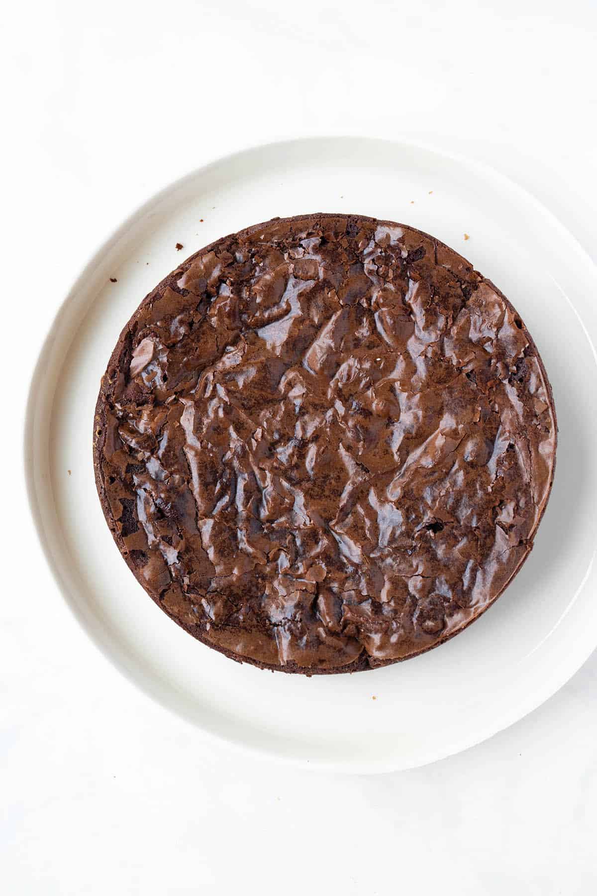 A homemade brownie with a very crinkly top sitting on a white plate.