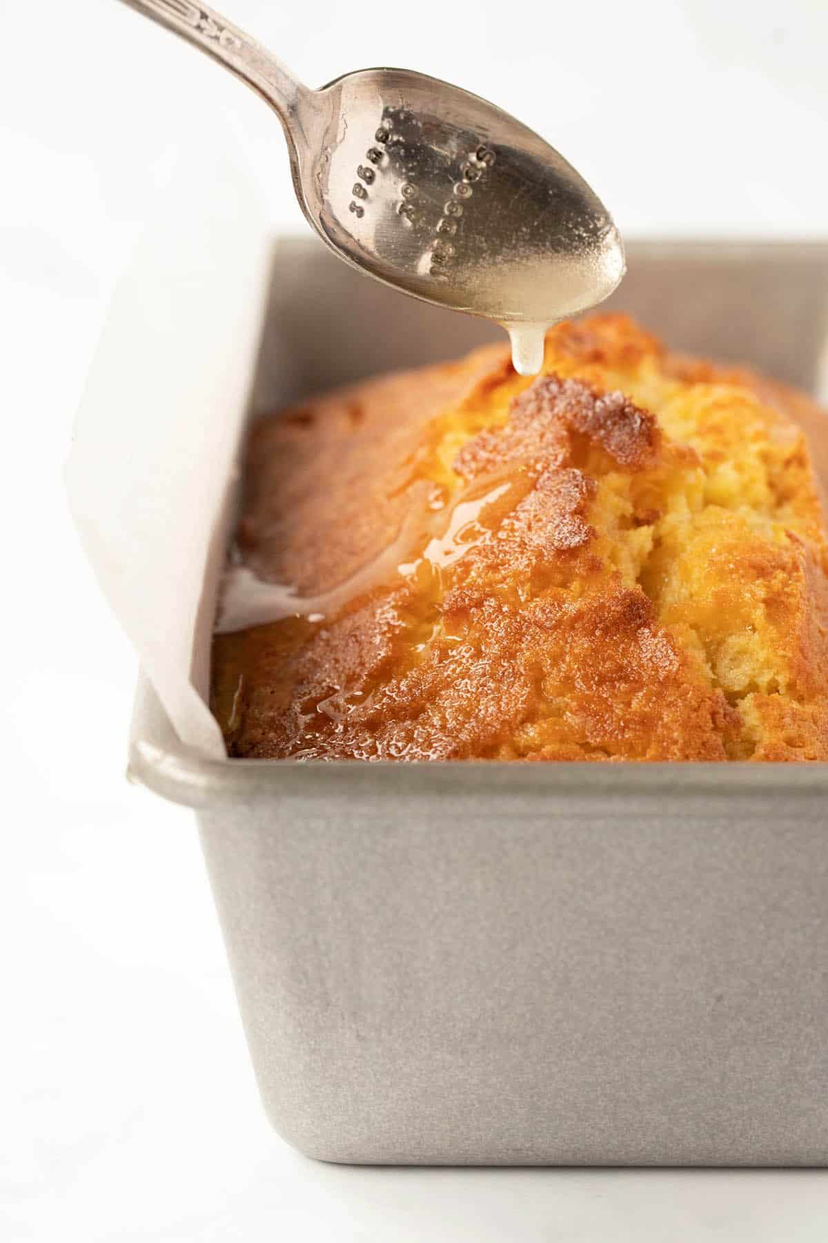 Close up a of a homemade Orange Pound Cake being drizzled with orange syrup.