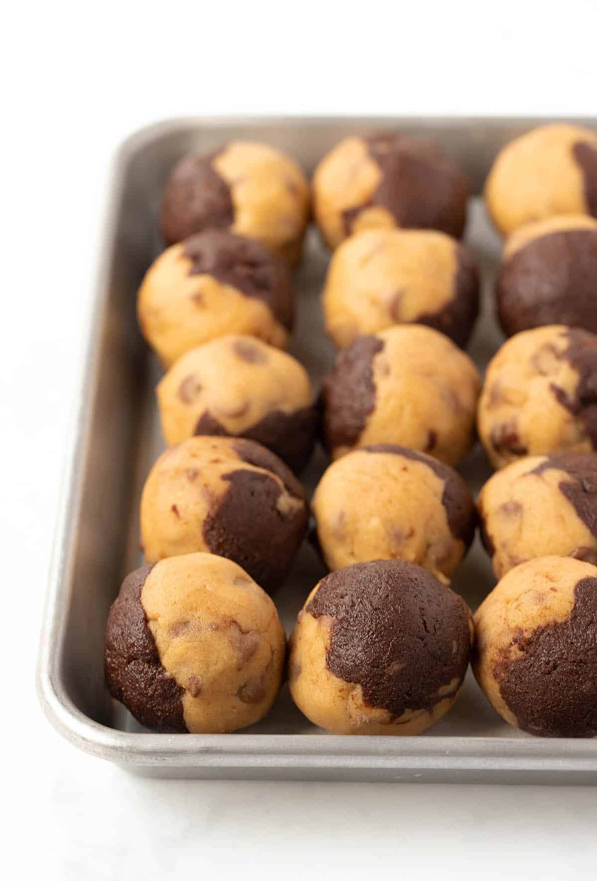Rolled balls of cookie dough on a silver baking tray. 
