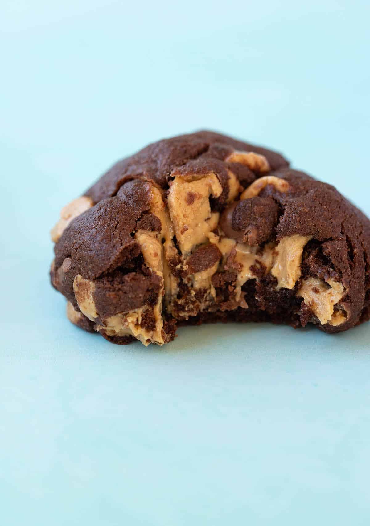 Close up of a gooey Chocolate Cookie filled with peanut butter chips on a blue background. 