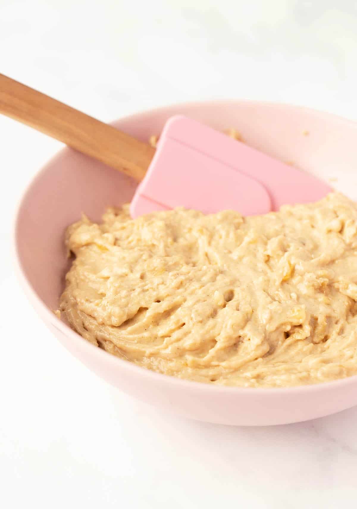 A pink bowl filled with gooey banana cake batter. 