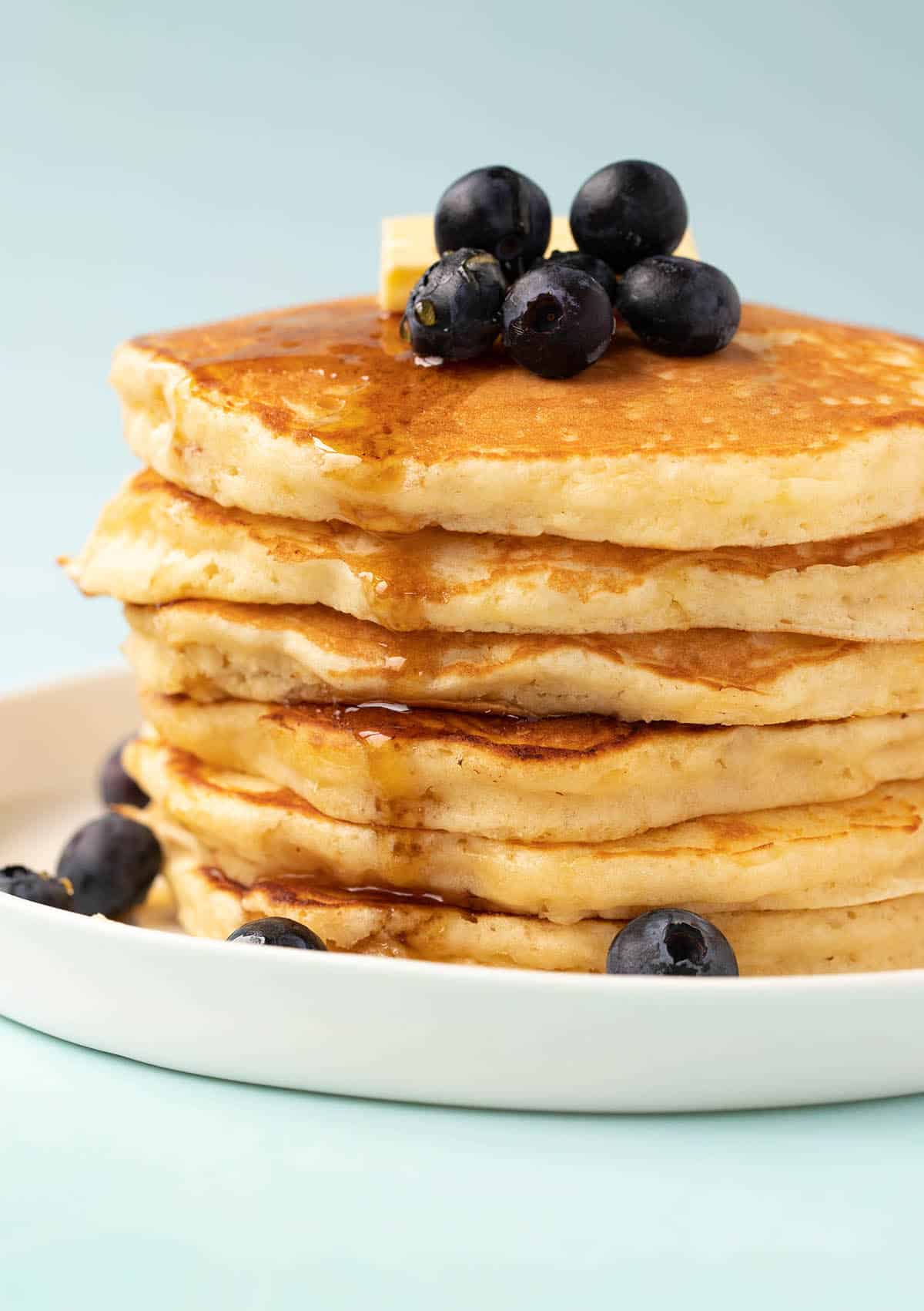 A stack of buttermilk pancakes decorated with maple syrup and blueberries.