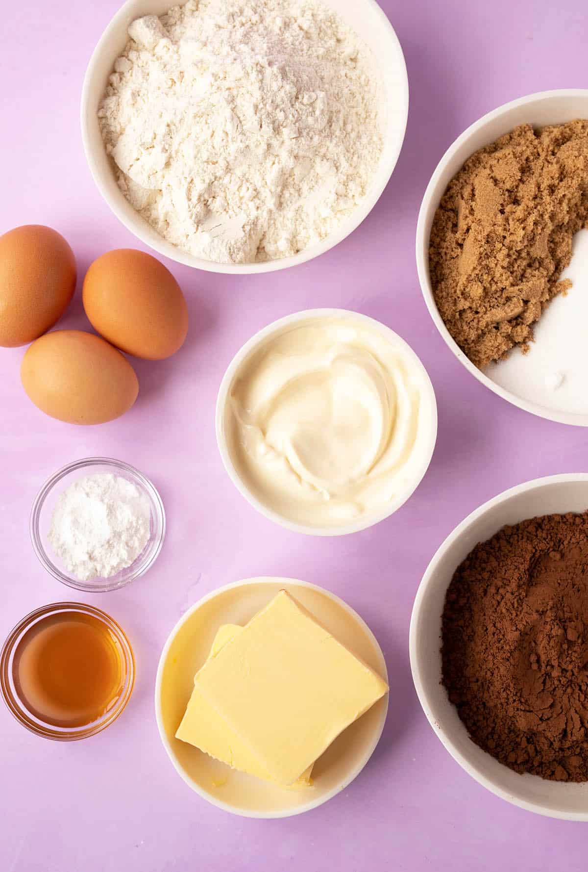 All the ingredients needed to make a chocolate cake from scratch on a purple background. 