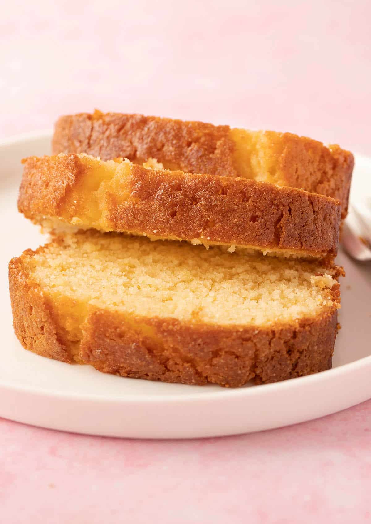Slices of a homemade Lemon Syrup Cake sitting on a white plate.