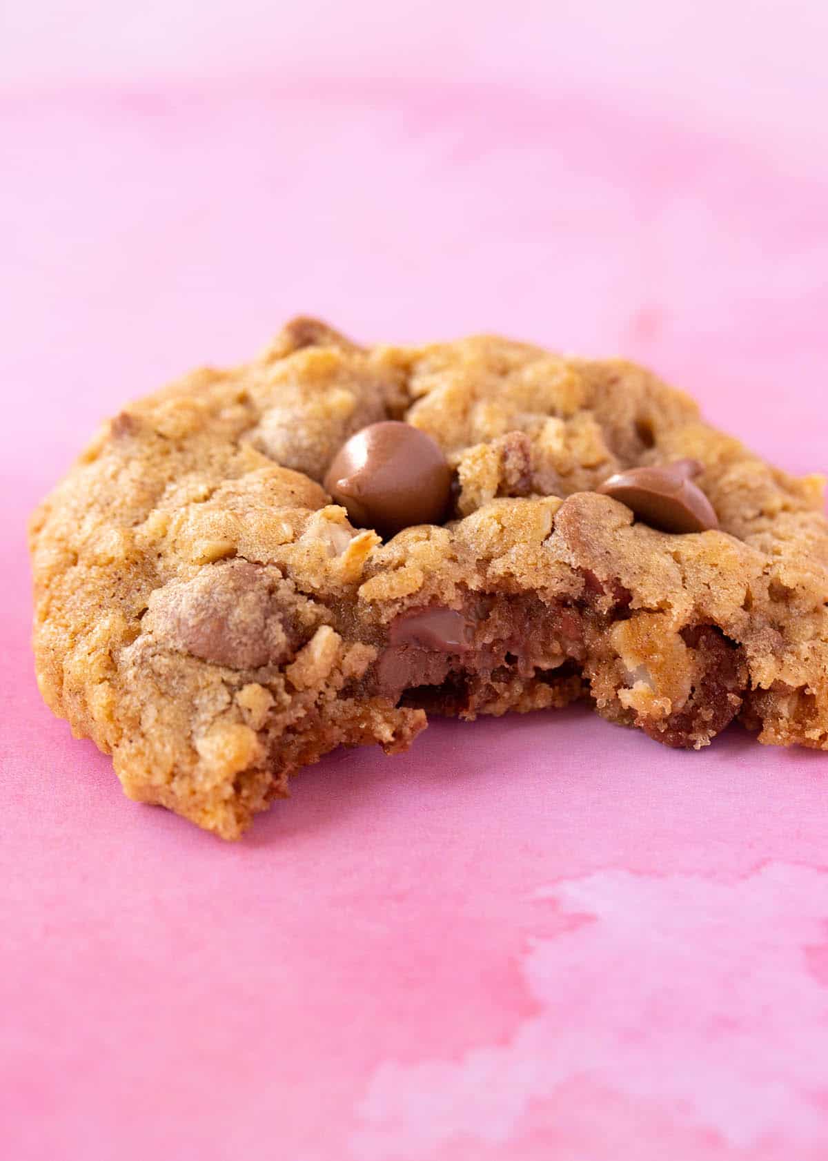 A close up of a chewy Oatmeal Chocolate Chip Cookie on a pink background.