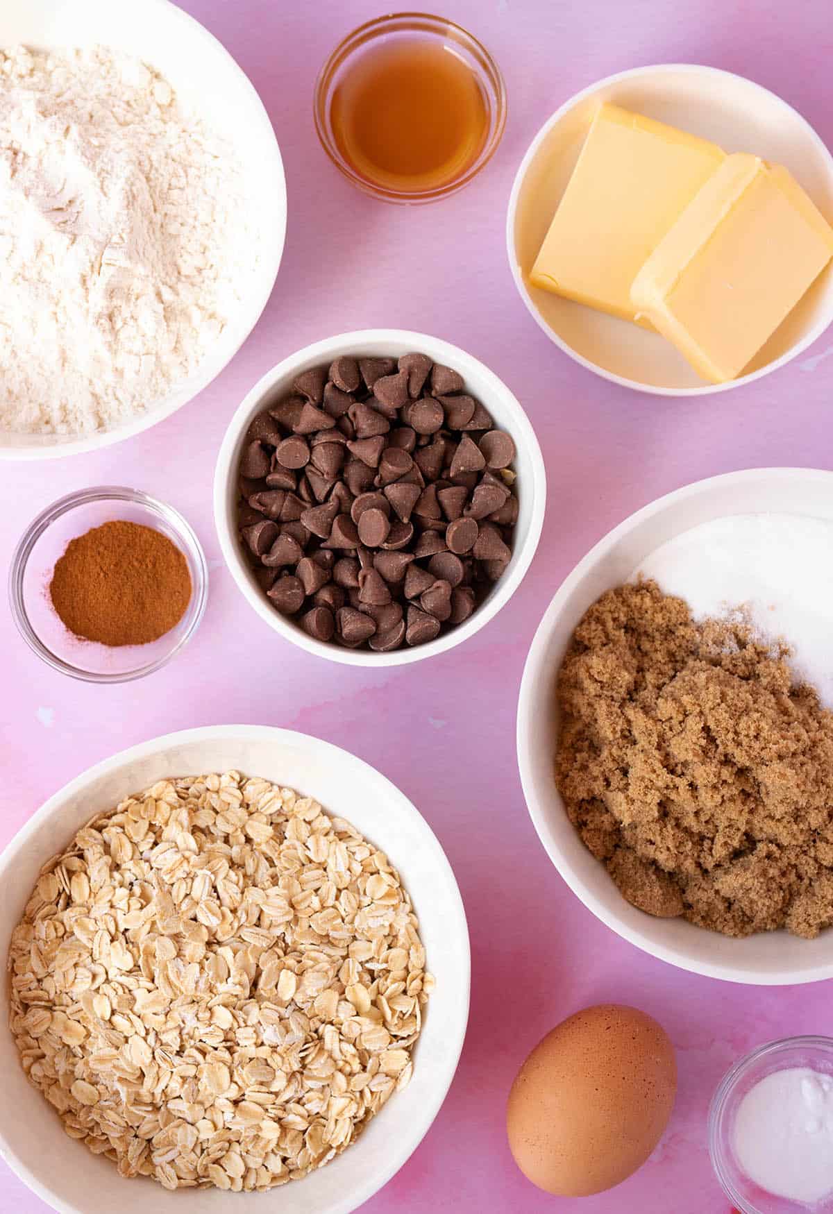 All the ingredients needed to make Oatmeal Chocolate Chip Cookies sitting on a pink background. 