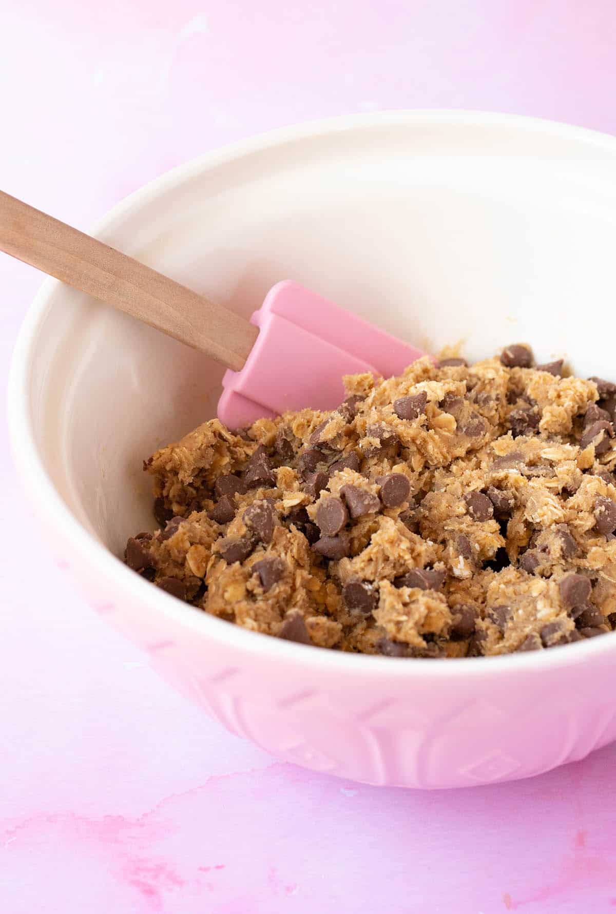 A pink mixing bowl filled with Oatmeal Chocolate Chip cookie dough. 