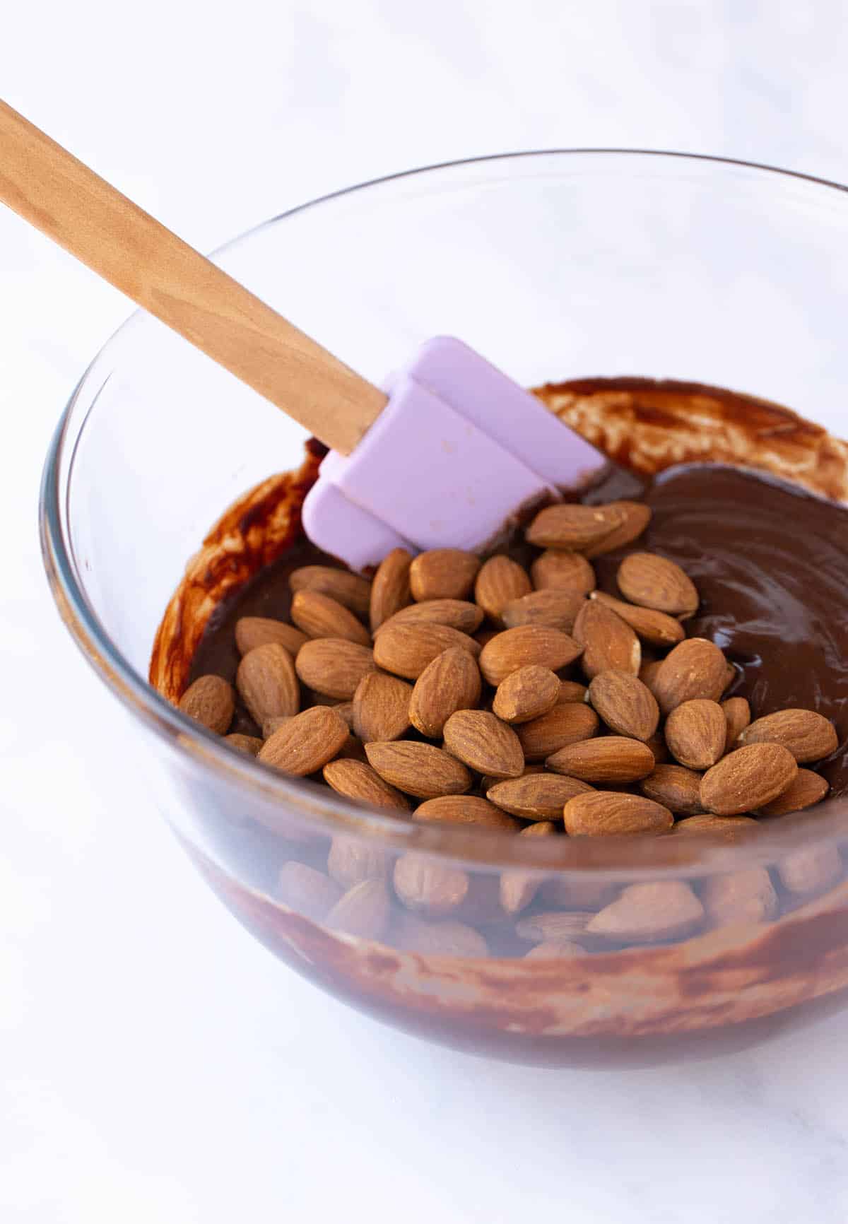 A glass bowl filled with chocolate fudge batter and almonds.