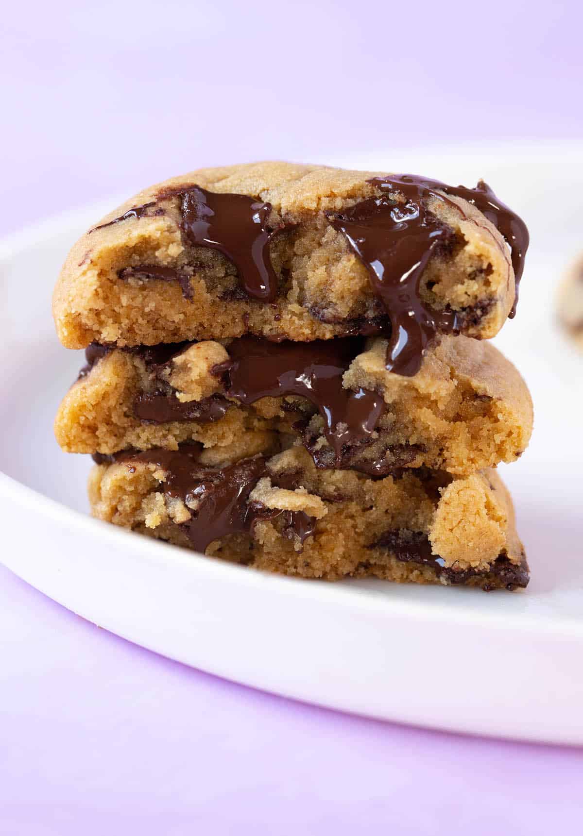 A tall stack of gooey Peanut Butter Chocolate Chip Cookies on a purple backdrop.