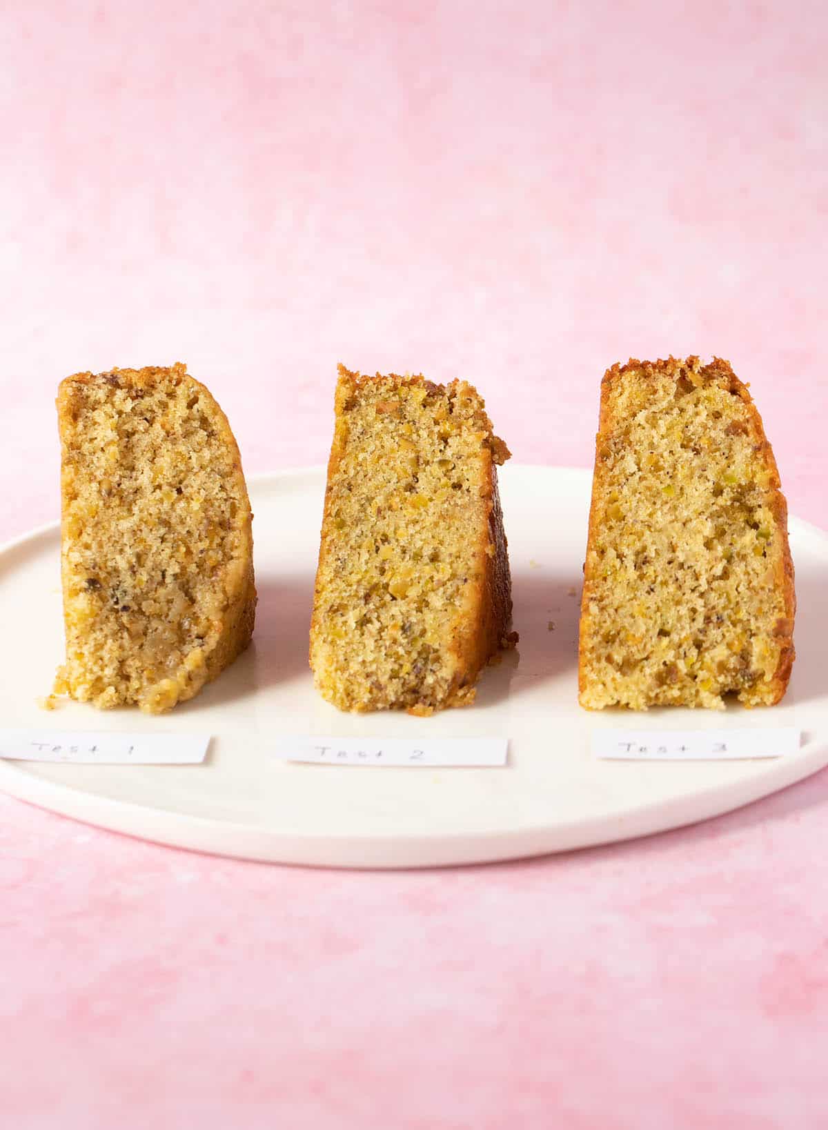 Three different slices of Pistachio Cake sitting on a pink background.