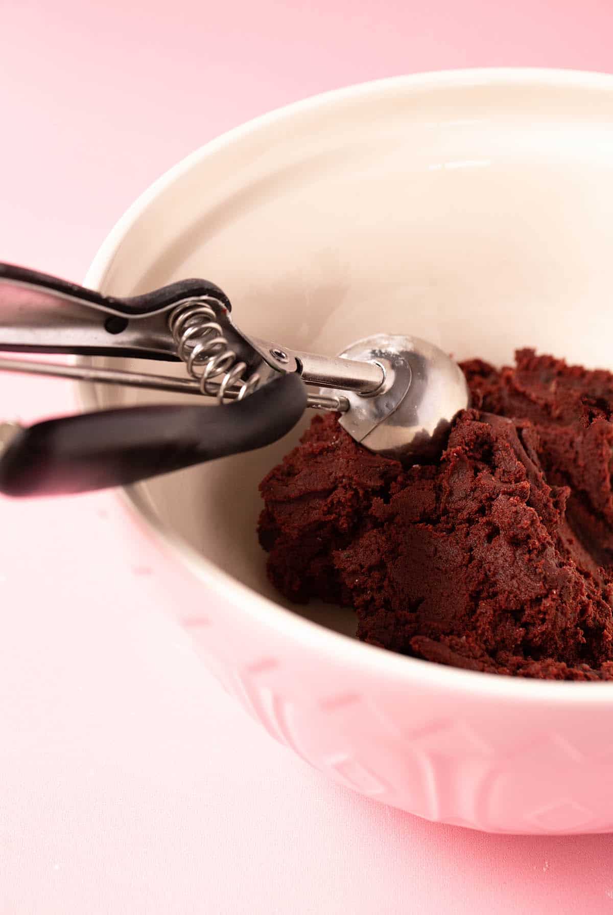 Red velvet cookie dough in a pink bowl with a standard cookie scoop.