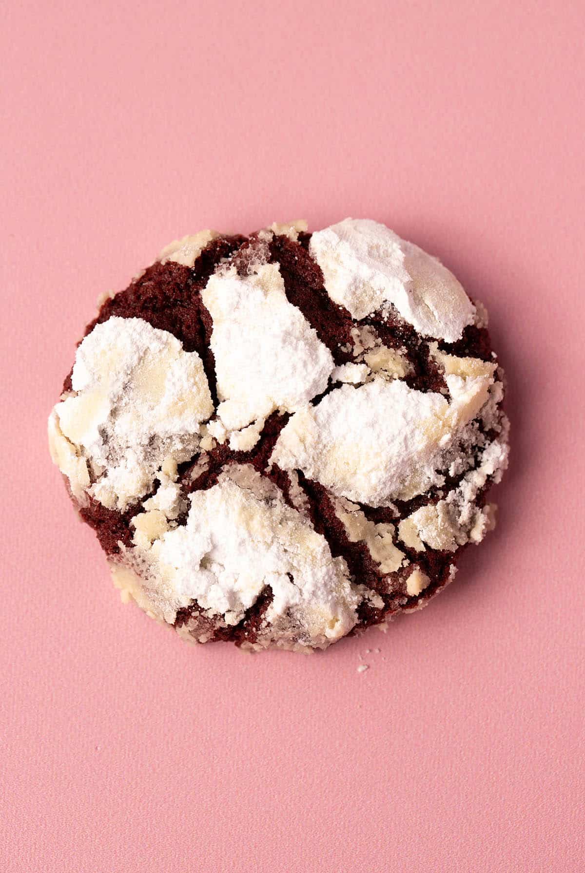 Close up of a beautiful homemade Red Velvet Crinkle Cookie on a pink backdrop.