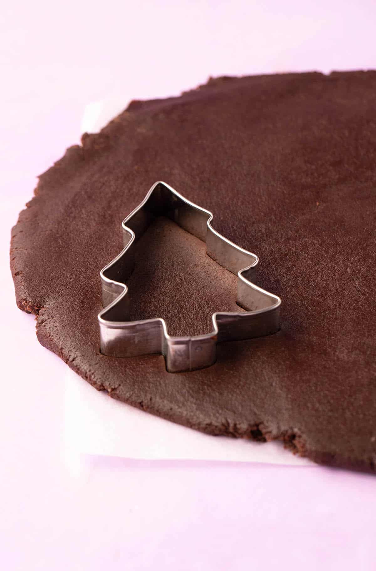 Chocolate cookie dough that’s been rolled with a Christmas tree cookie cutter ready to stamp. 