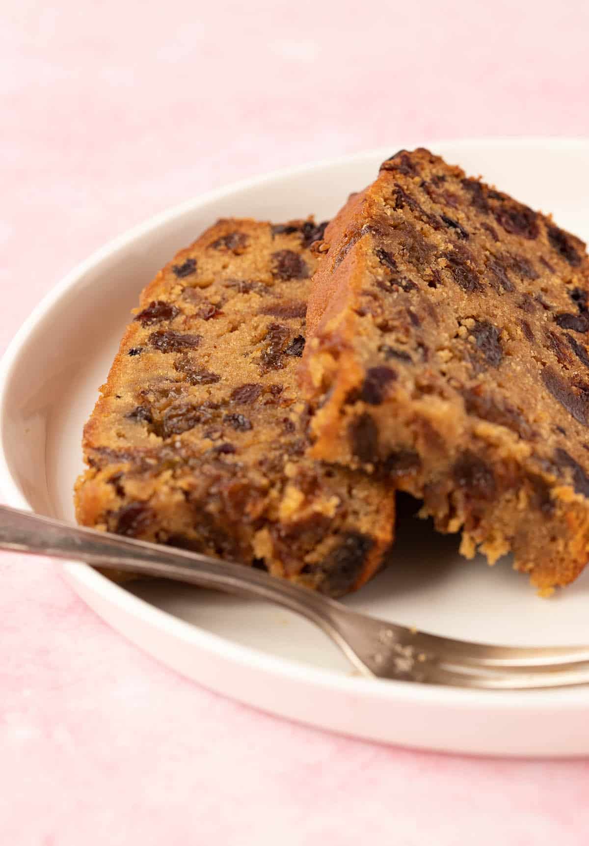Two slices of Fruit Cake on a white plate with a small fork.