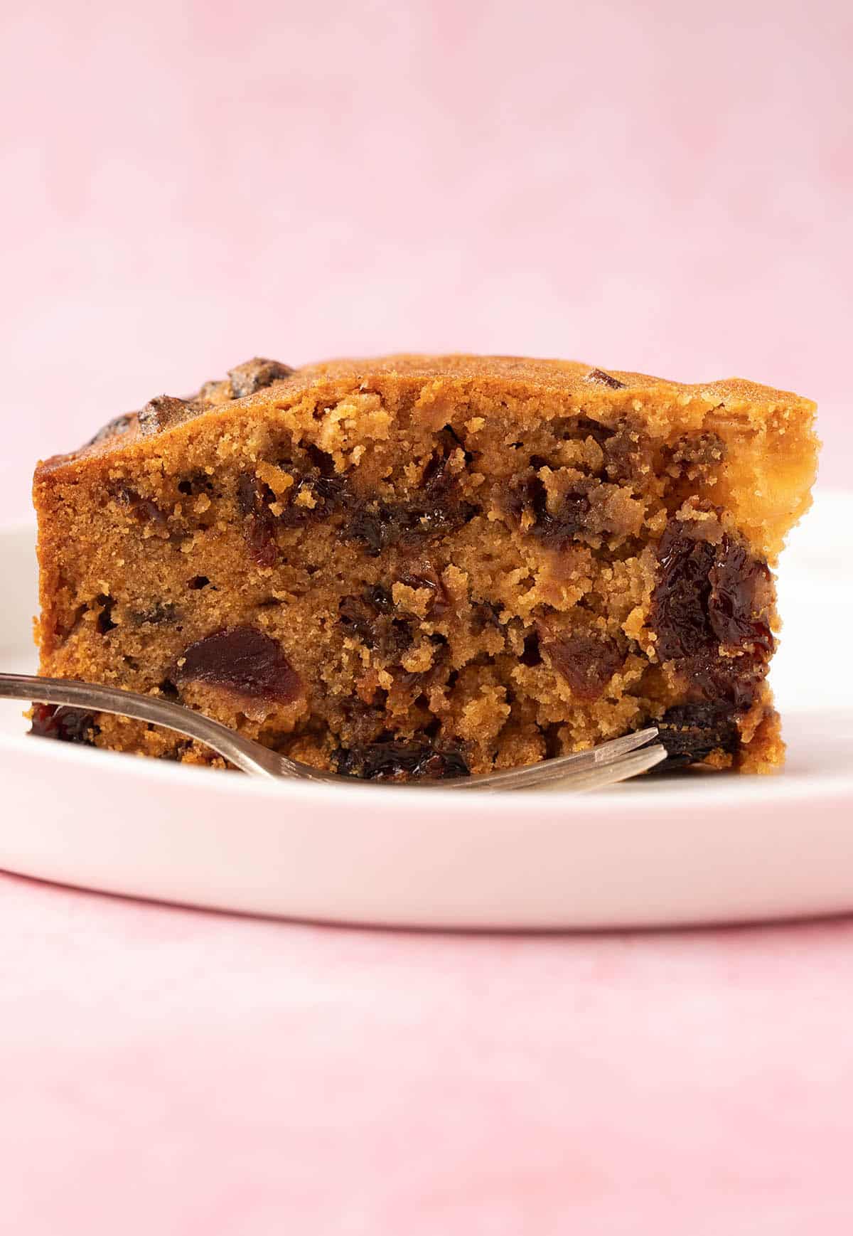 A close up photo of a beautiful slice of Easy Fruit Cake on a white plate. 