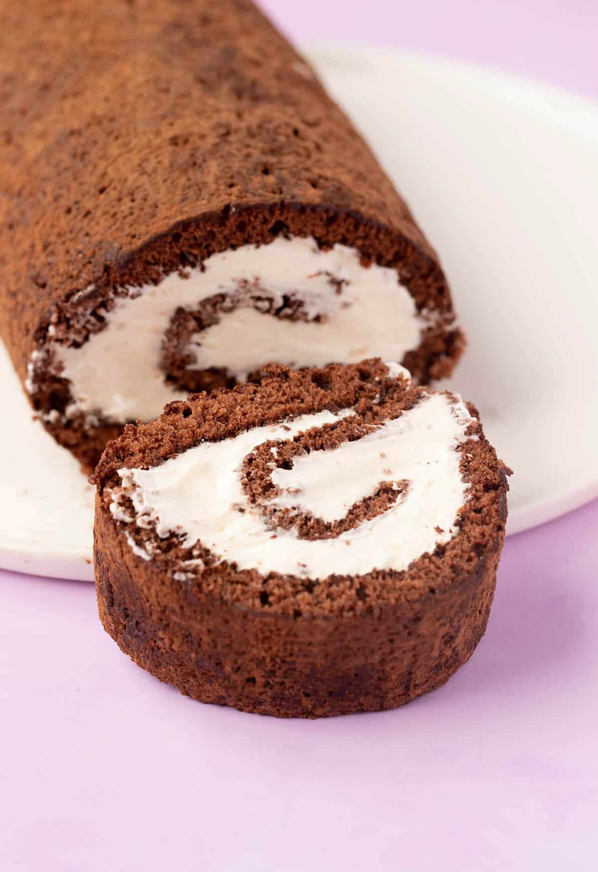 A slice of Chocolate Swiss Roll filled with whipped cream on a white plate. 