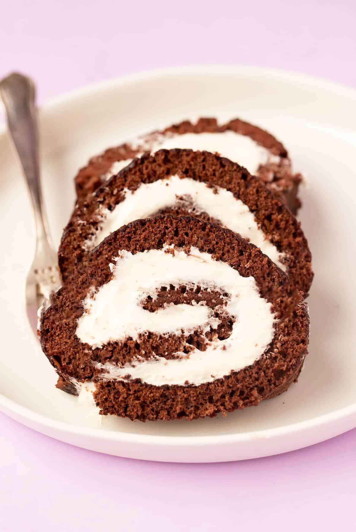 Slices of chocolate swiss roll sitting on a white plate with a small fork.