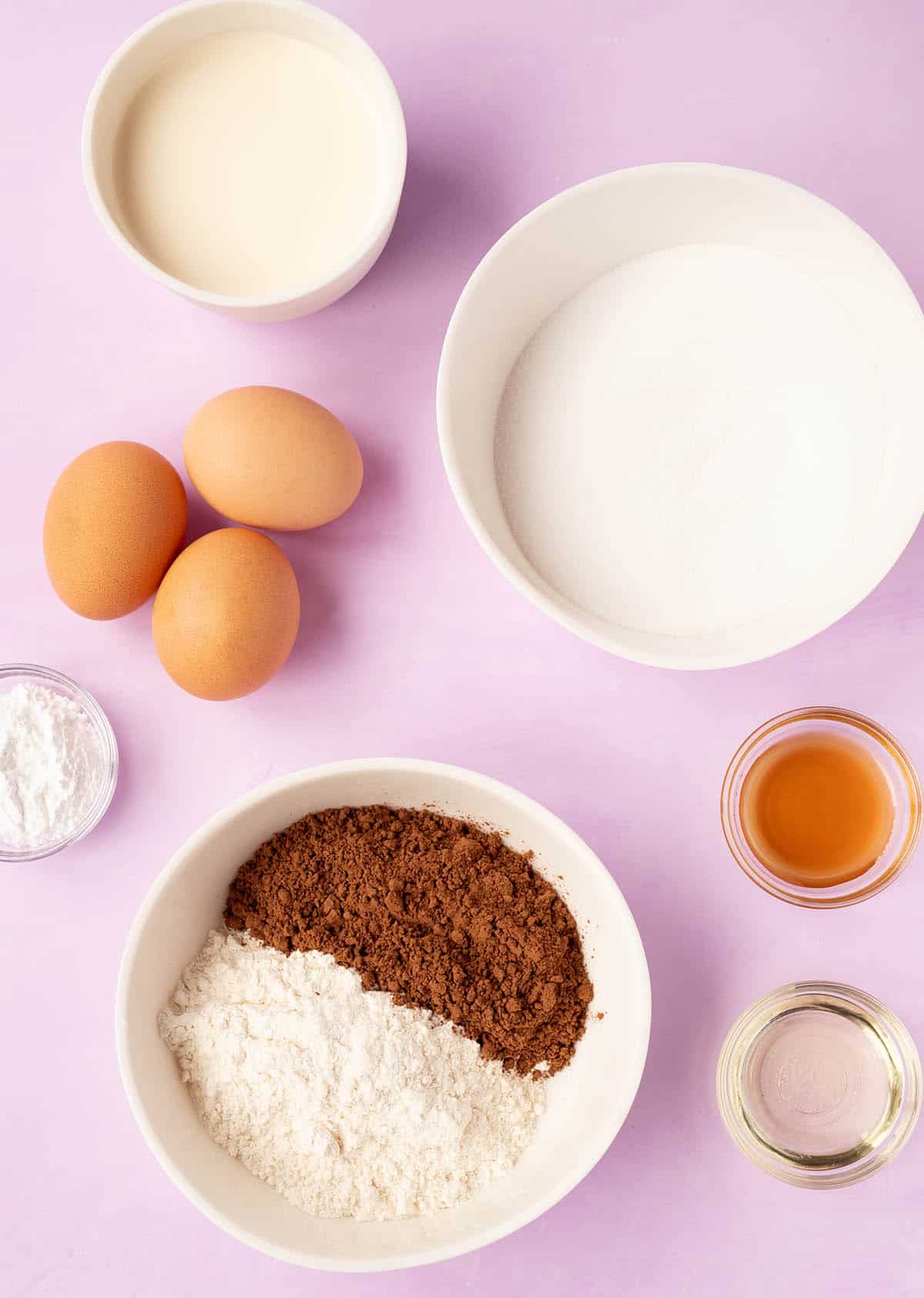 All the ingredients needed to make a Chocolate Cake Roll from scratch on a purple backdrop. 