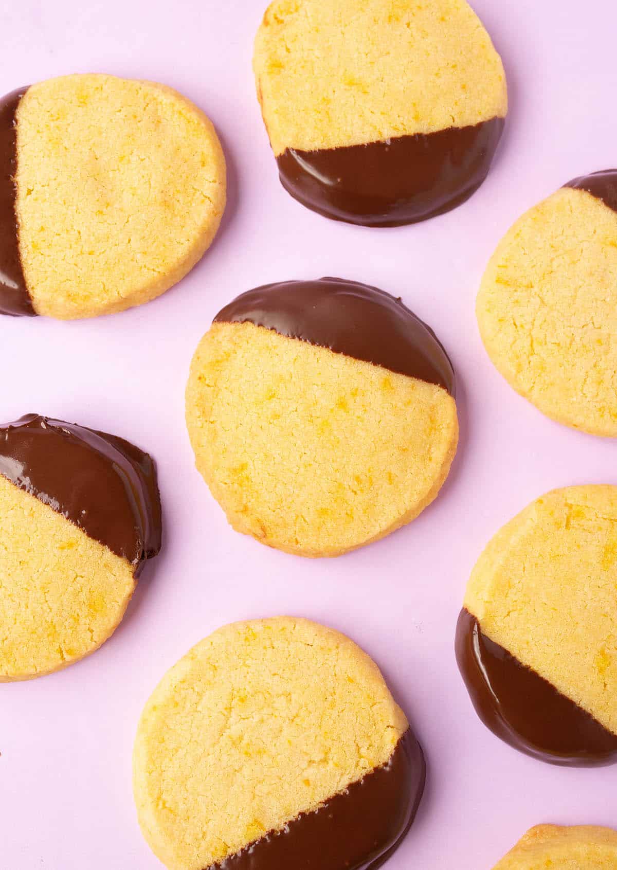 Top view of buttery Orange Cookies dipped in dark chocolate on a purple backdrop.