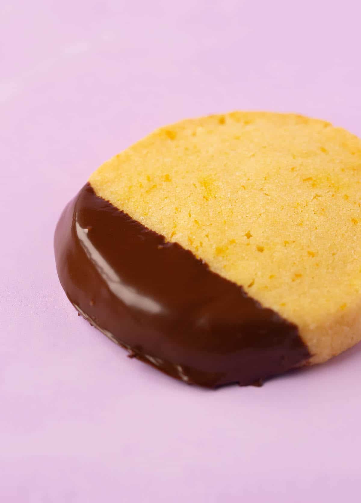 Close up of a chocolate dipped Orange Cookie on a purple backdrop.