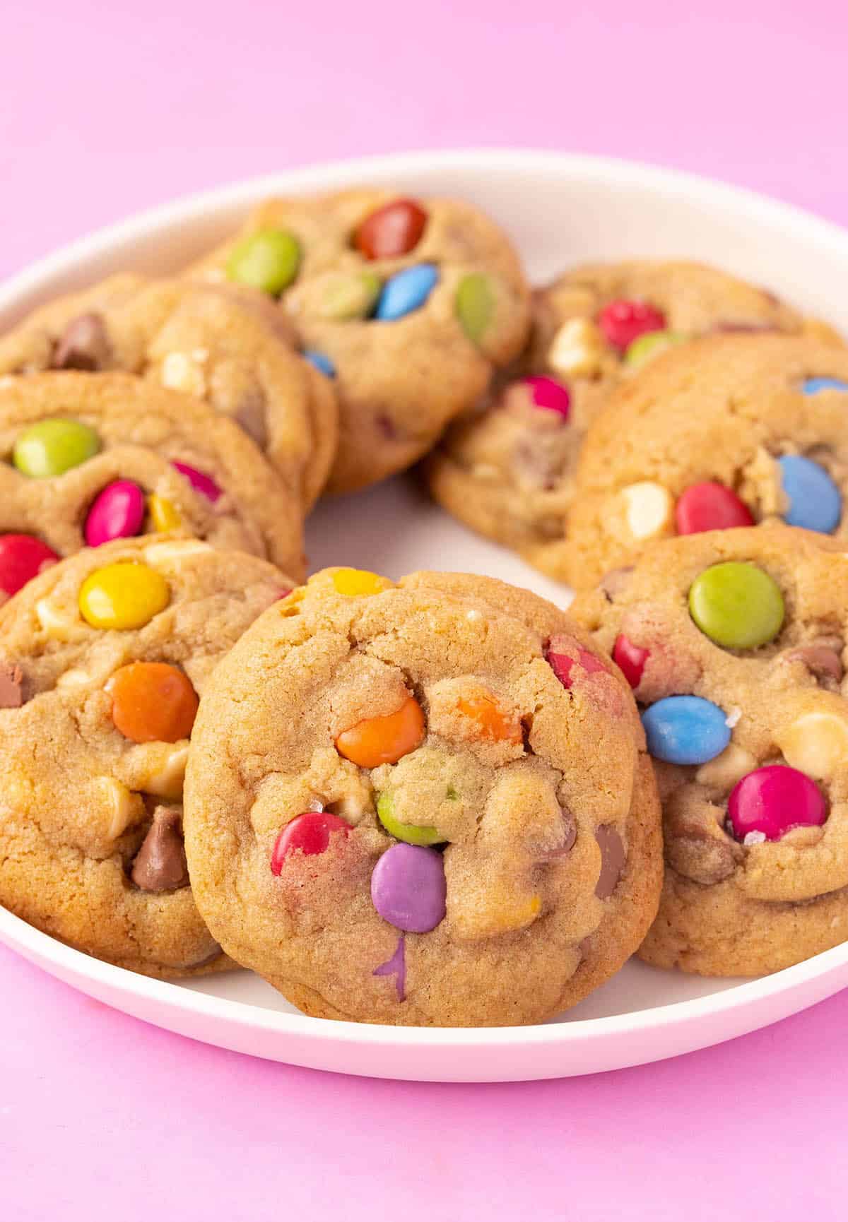 A plate of soft and chewy Smartie Cookies on a pink background. 