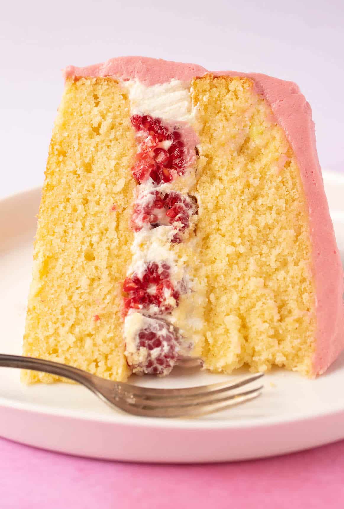 A beautiful slice of Lemon Raspberry Cake on a pink backdrop.