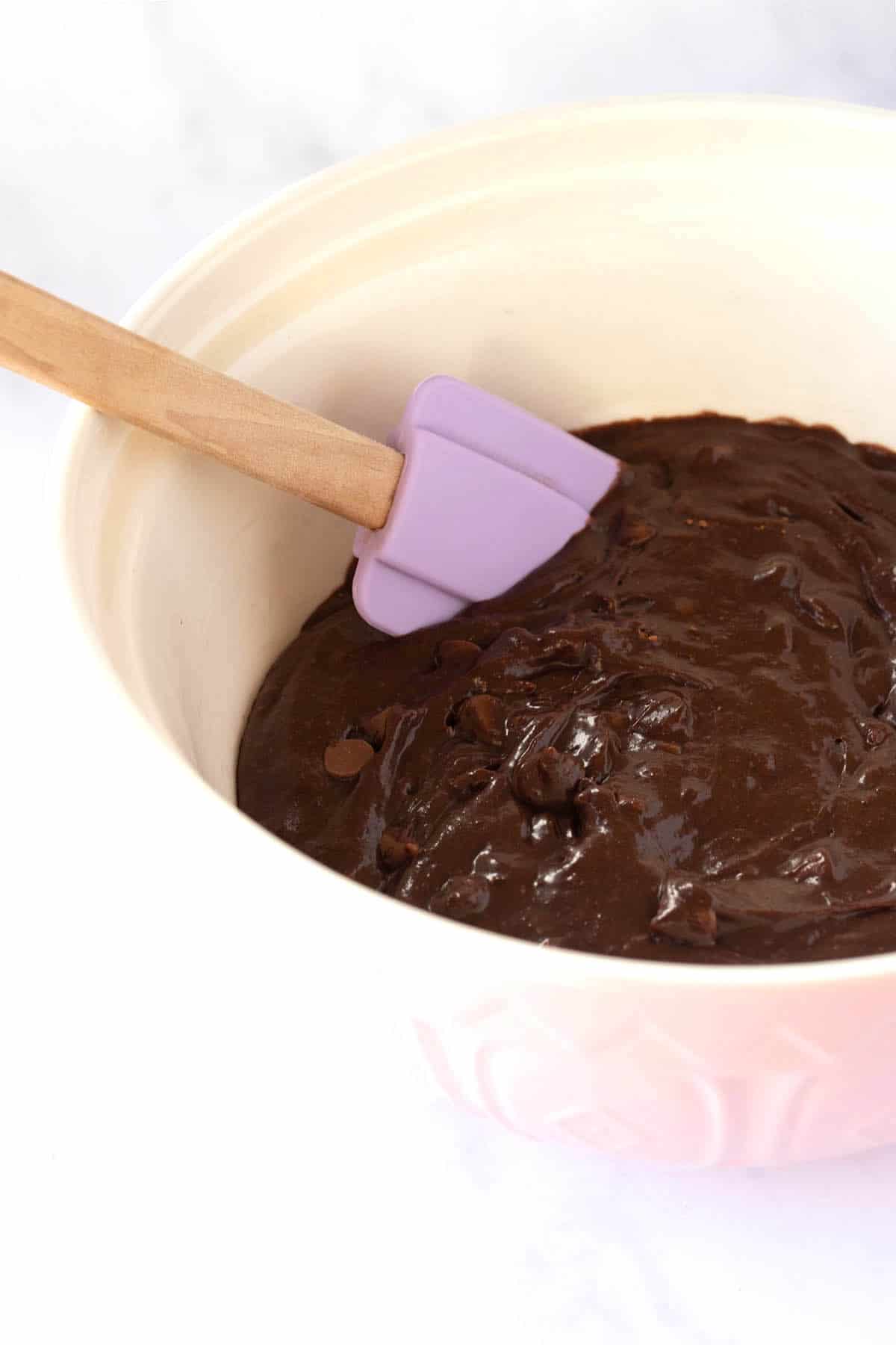 A large mixing bowl filled with gooey chocolate brownie batter and a purple spatula. 