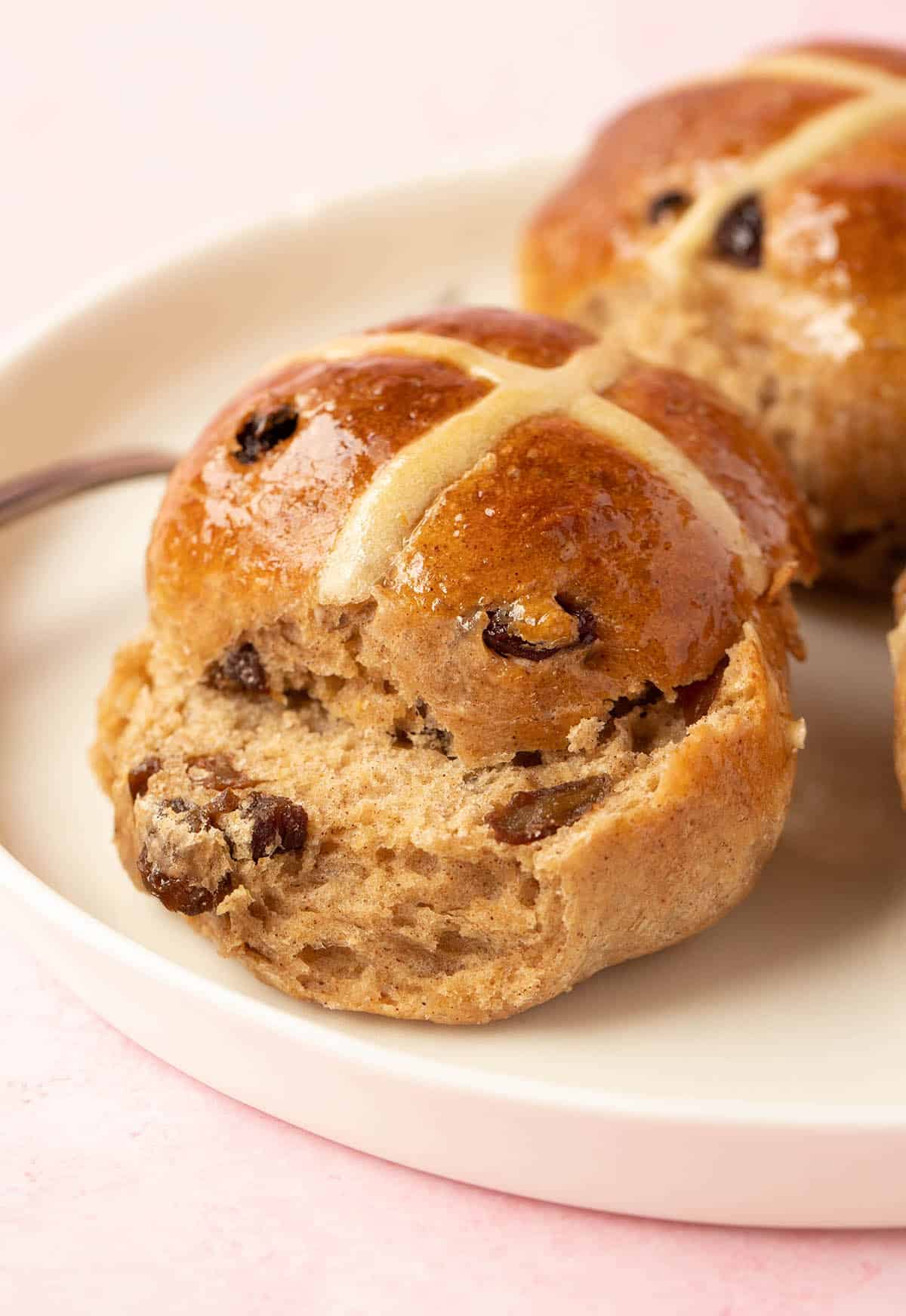 Homemade Hot Cross Buns sliced open to reveal soft crumb on a white plate. 