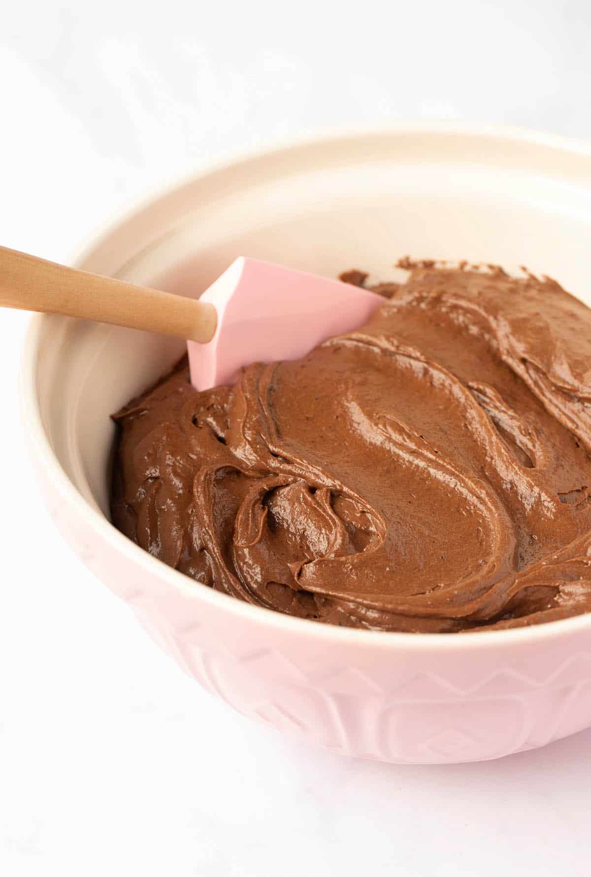 A pink mixing bowl filled with chocolate cake batter.