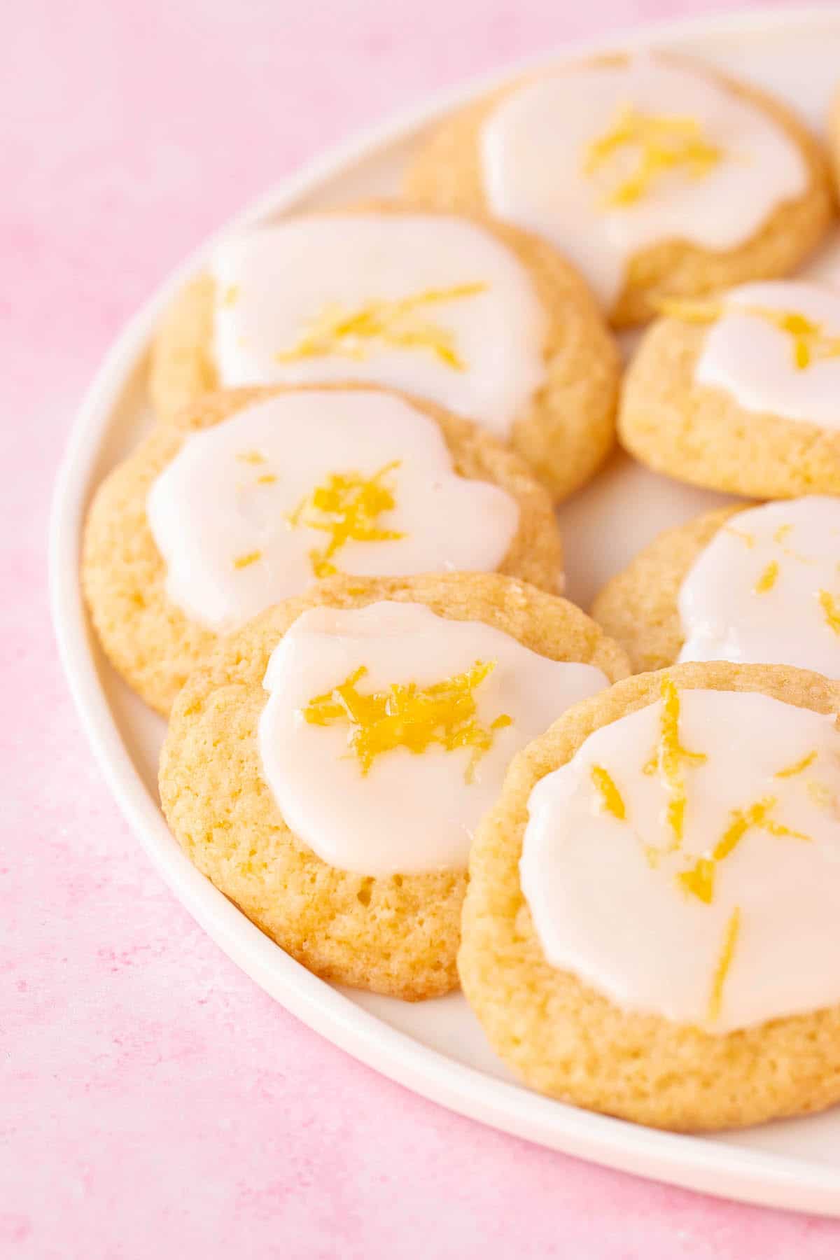 A white plate filled with Lemon Ricotta Cookies decorated with a lemon glaze.