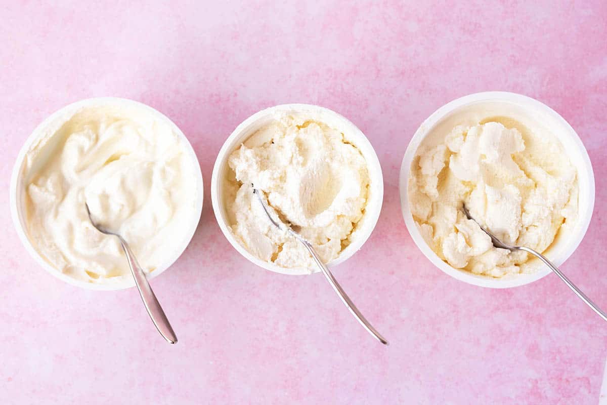 Three different tubs of storebought ricotta cheese on a pink background.
