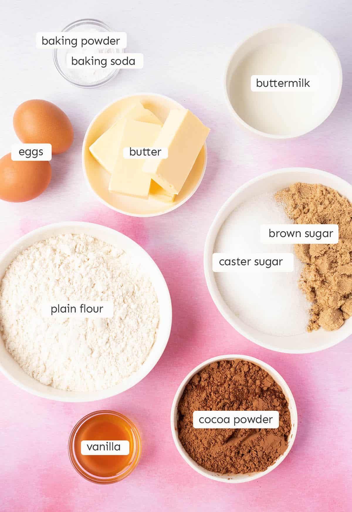 All the ingredients needed to make chocolate buttermilk cake from scratch on a pink background.