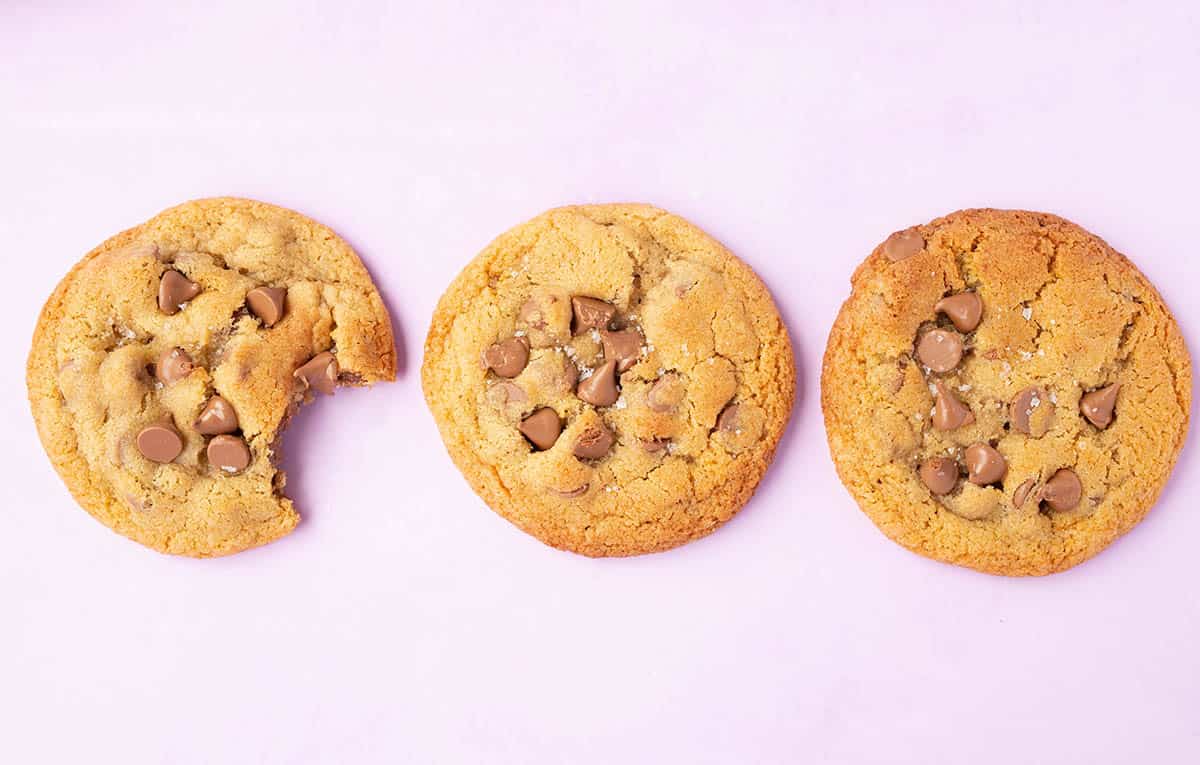 Three golden chocolate chip cookies on a purple backdrop.
