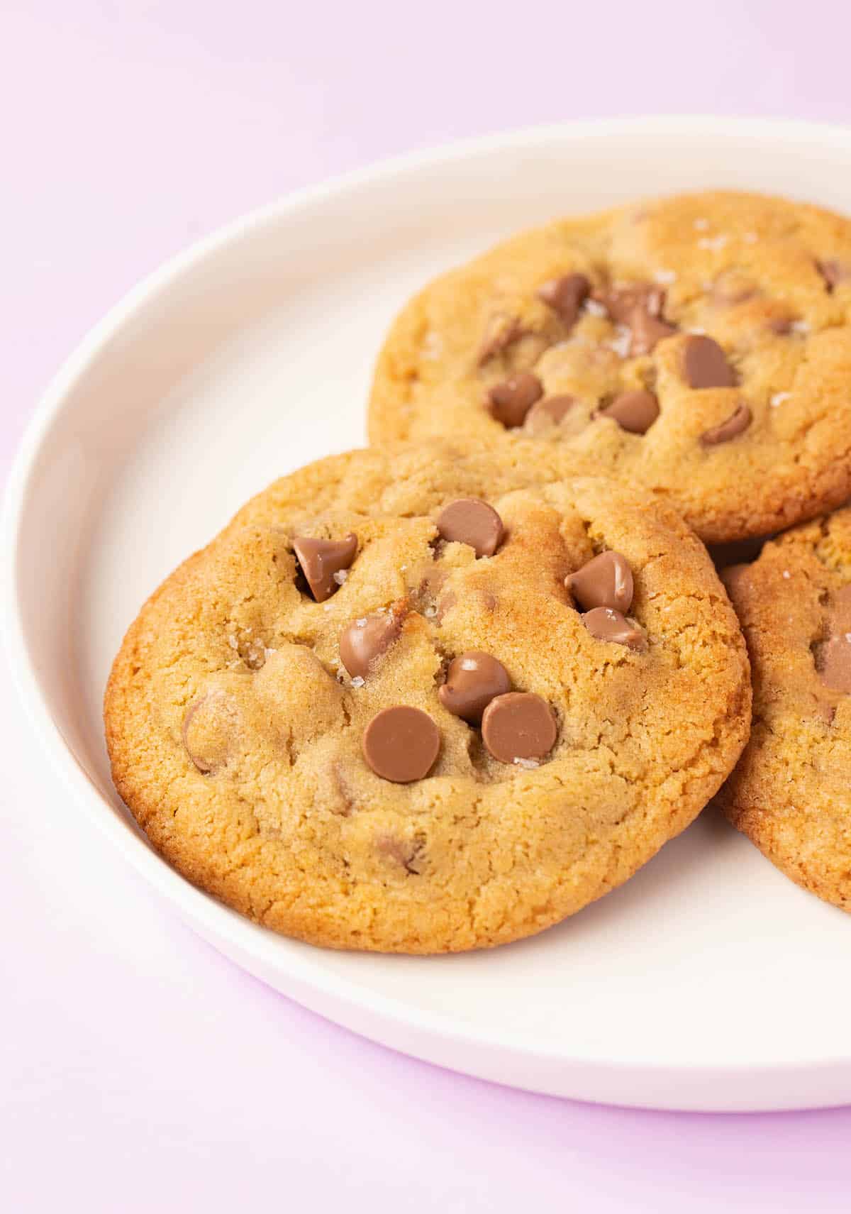 A white plate with three chocolate chip cookies on it.