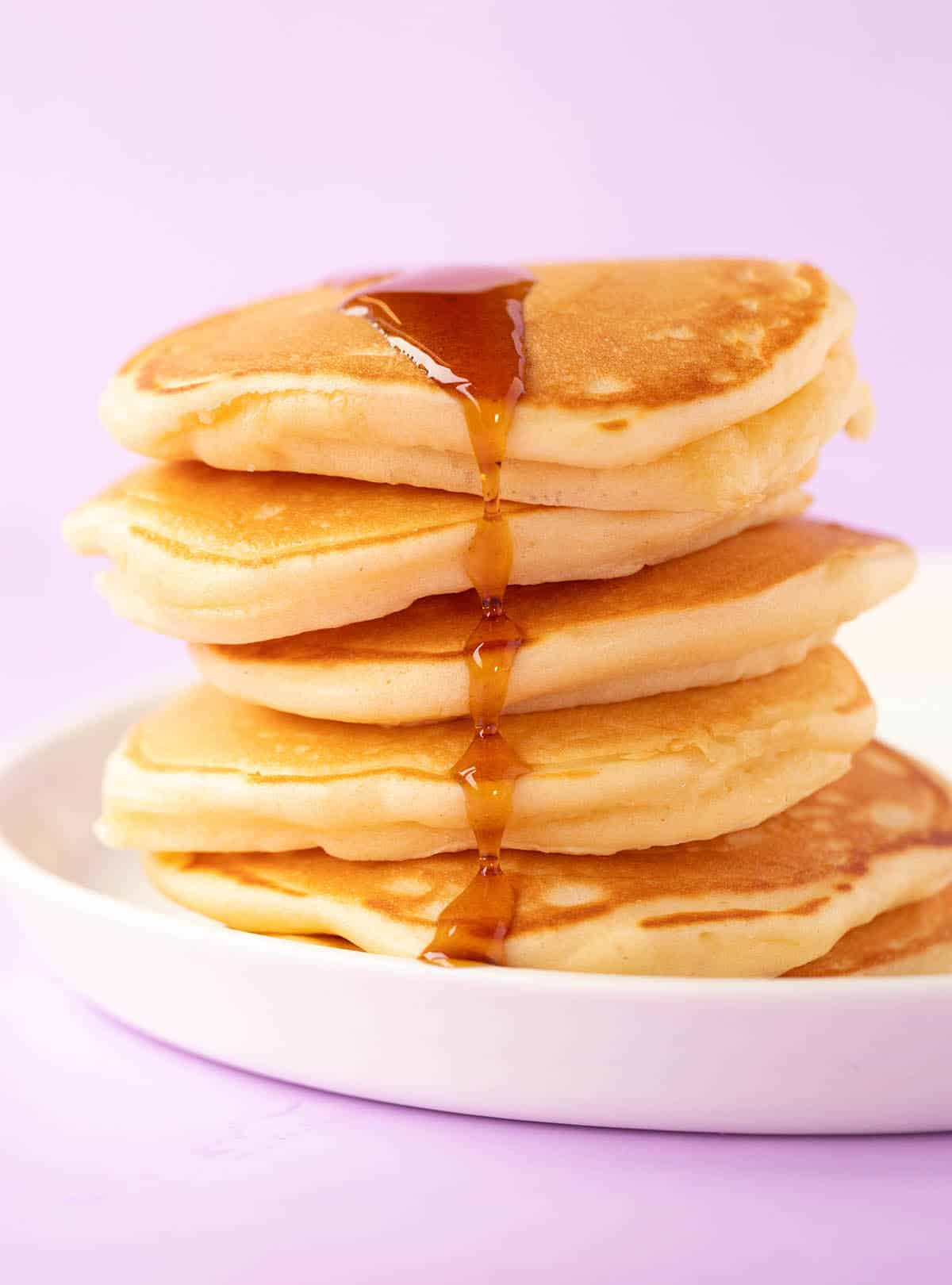 A stack of mini pancakes covered in maple syrup on a white plate. 