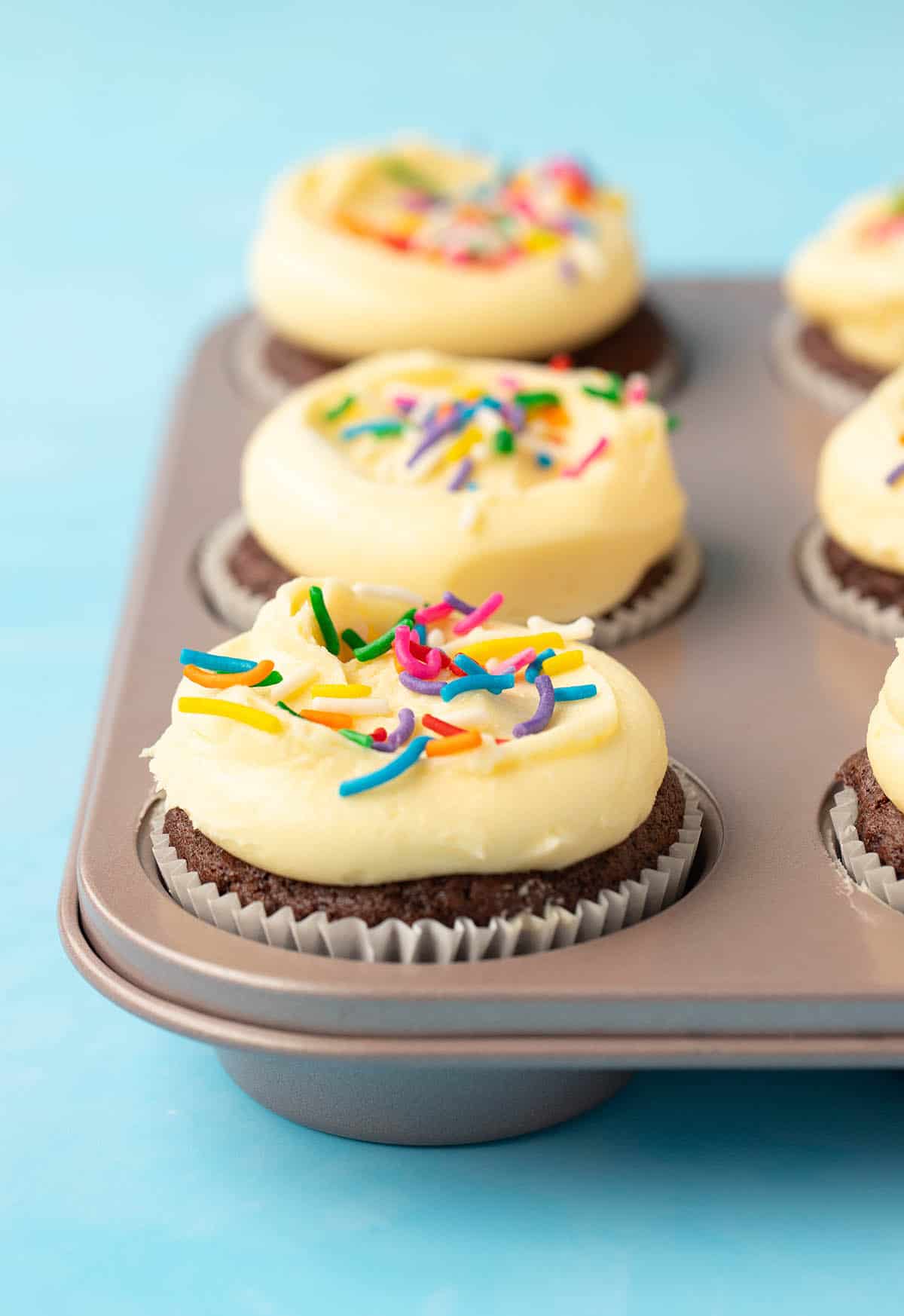 A muffin pan filled with small batch chocolate cupcakes topped with rainbow sprinkles. 