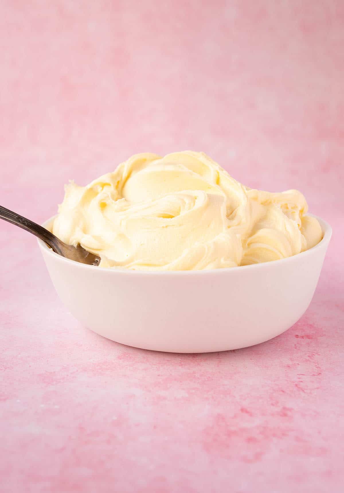 A white bowl filled with white chocolate buttercream on a pink background.