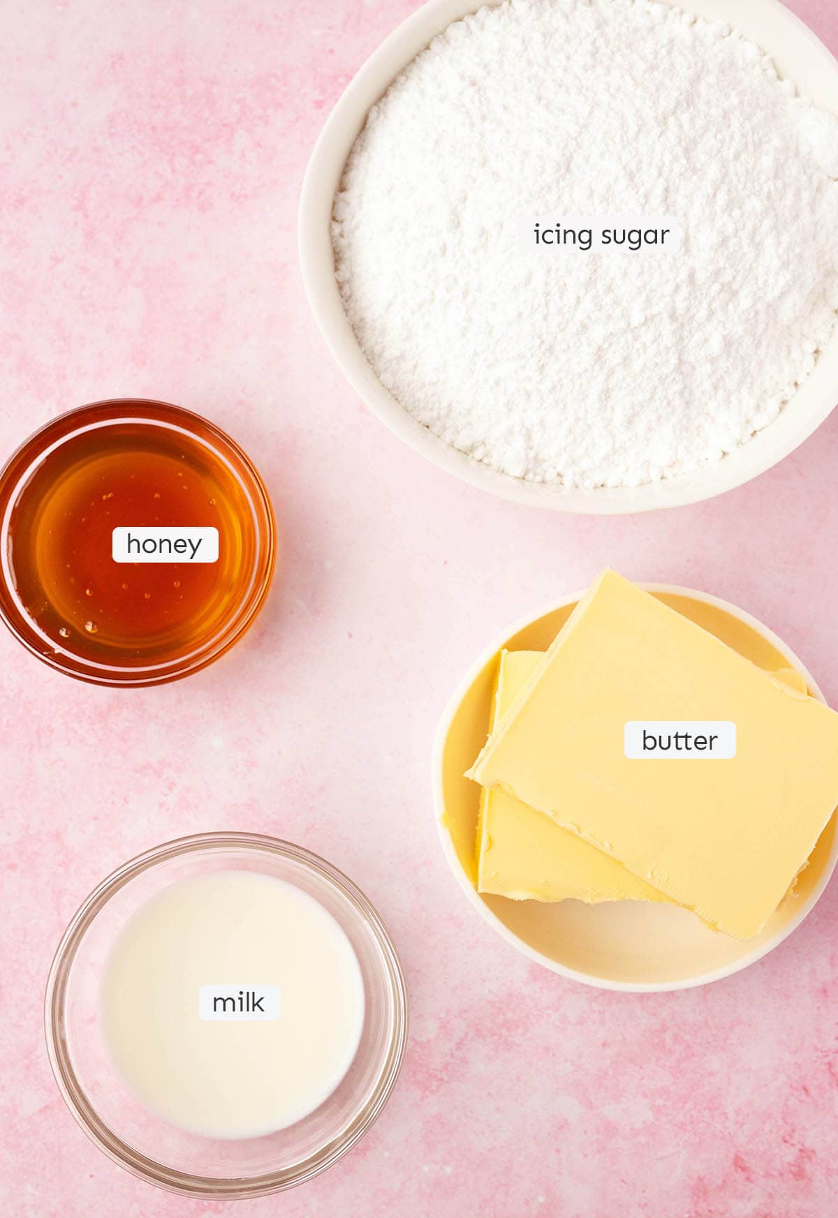 All the ingredients needed to make honey buttercream from scratch laid out on a pink backdrop.