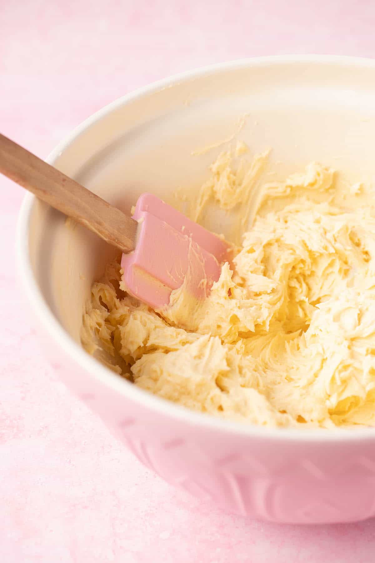 A pink mixing bowl filled with homemade honey buttercream. 